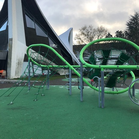 Spielplatzgerüst mit Gemeindehaus im Hintergrund.